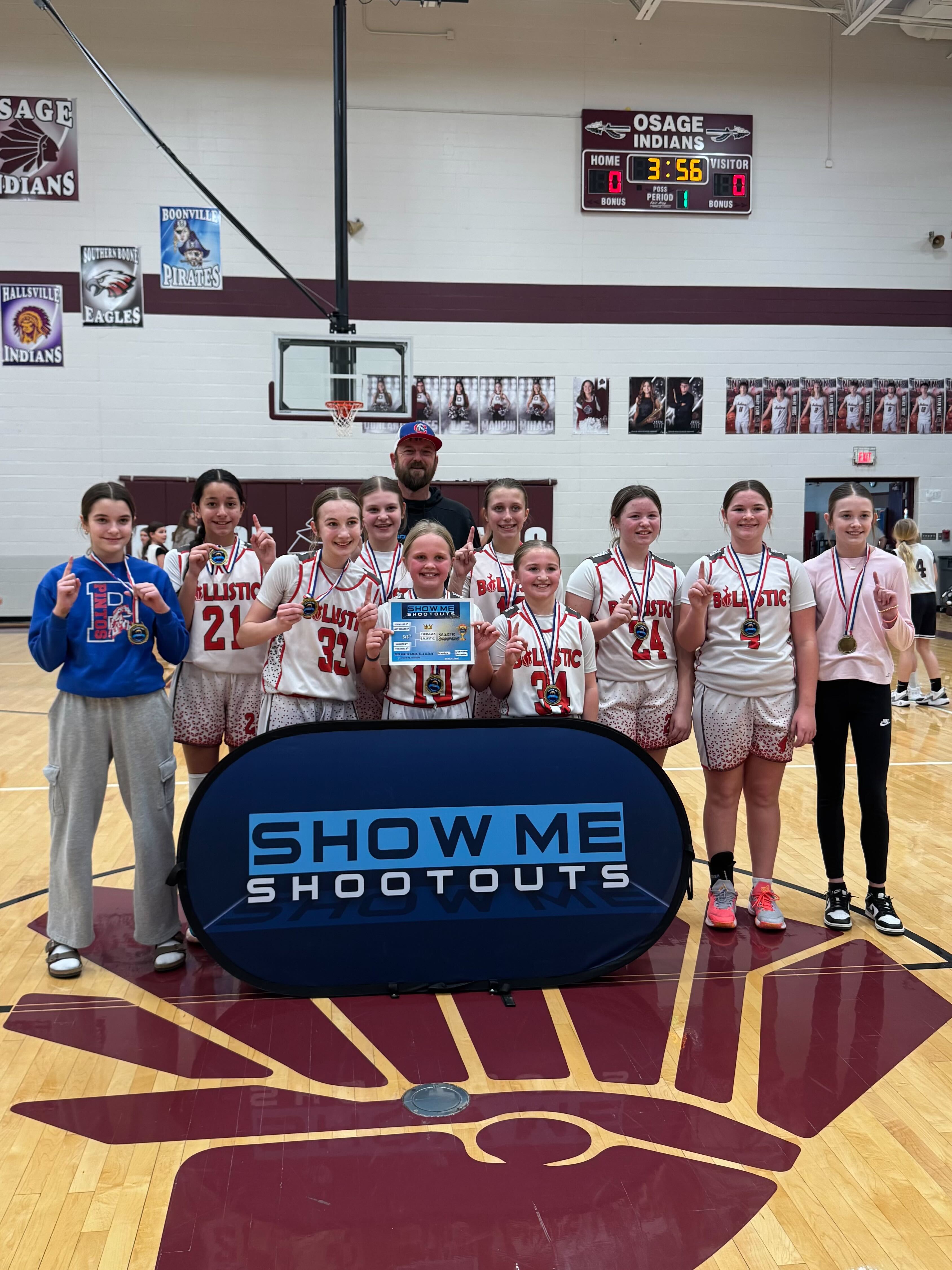 A girls Ballistic team celebrates a league championship with medals and a trophy card.