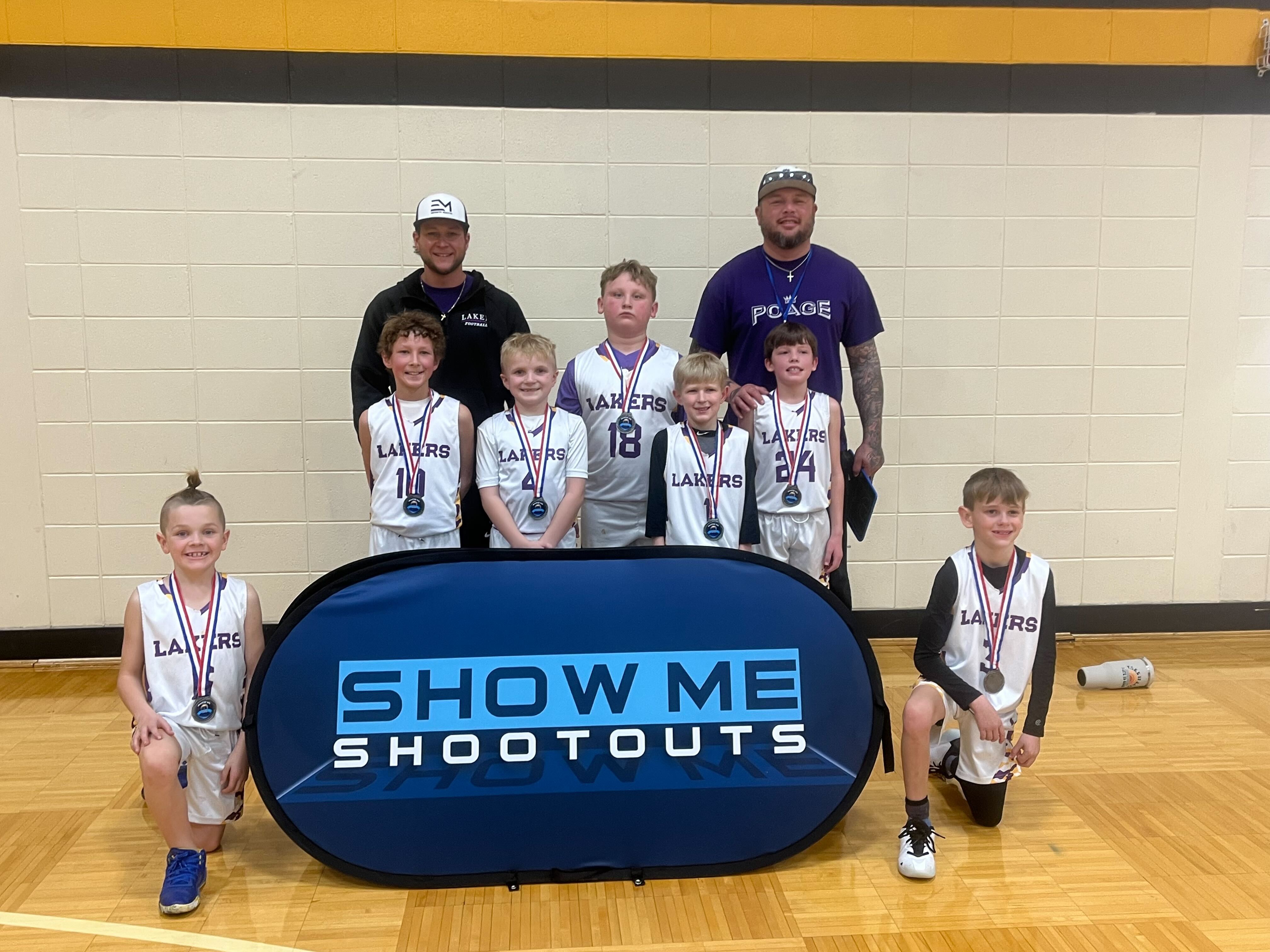 A young Lakers boys team celebrates with medals and coaches after a shootout.