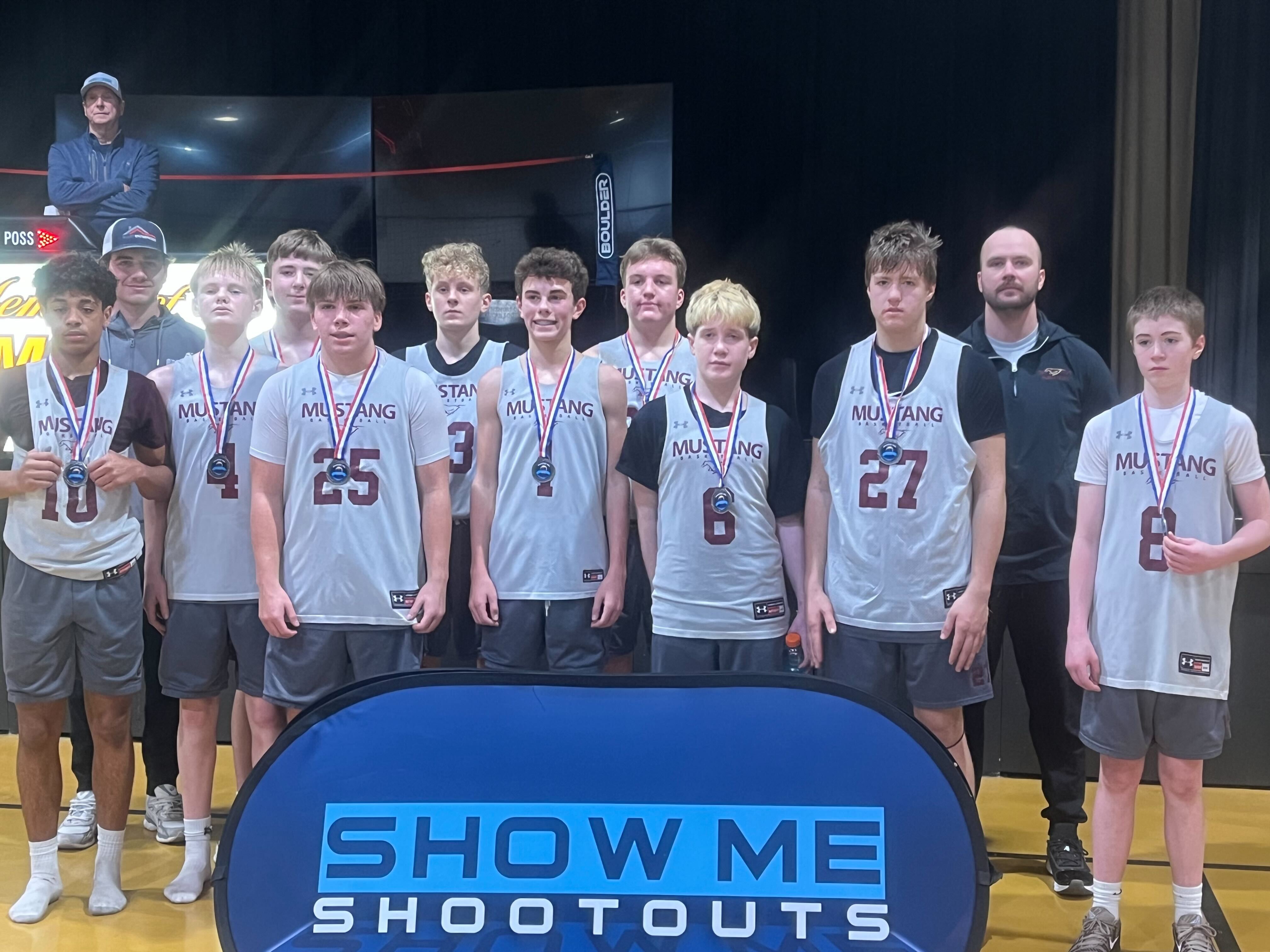 An older Mustang boys team lines up with their medals on the arena stage.
